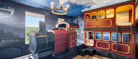 A room with a mural of a train, a chandelier, and a window with a view of a cityscape.