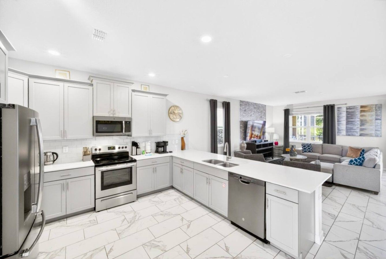 A modern kitchen with white cabinetry, a central island, and a dining area with a sofa and coffee table.