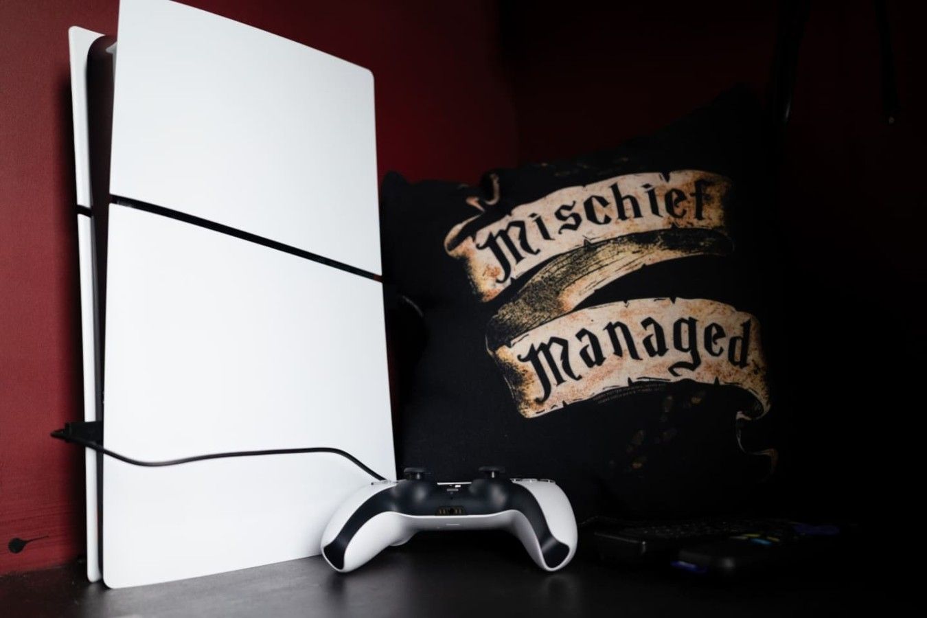 Een gaming opstelling met een wit scherm, een zwarte game controller en een zwart kussen met tekst.