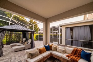 A covered outdoor seating area with a sofa and a small table, a pergola, and a view of the outdoors. - Ultimate 9BR Villa | Pool | Resort | Near Disney (Kissimmee)