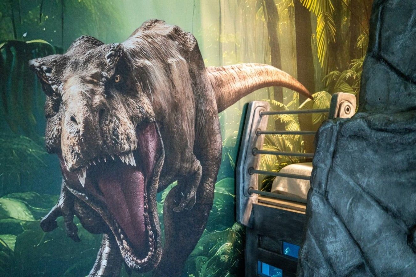 Ein Dinosaurier in einer naturgetreuen Ausstellung mit einer Metallreling und Vegetation im Hintergrund.