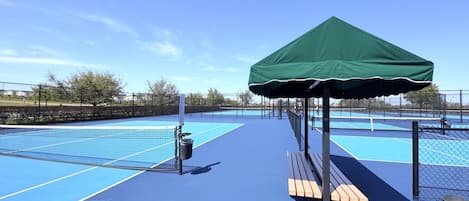 Un court de tennis avec un pavillon vert, des bancs et une poubelle.