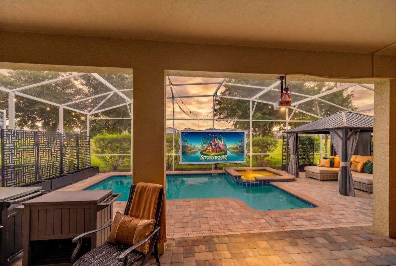 A covered outdoor swimming pool area with a patio, seating, and a view of a Storybook-themed mural.