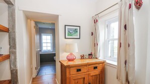 Ein Flur mit Holzboden, einem Holzkabinett mit Schubladen, einer Wandlampe, einem gerahmten Bild und einem Fenster mit Vorhängen.