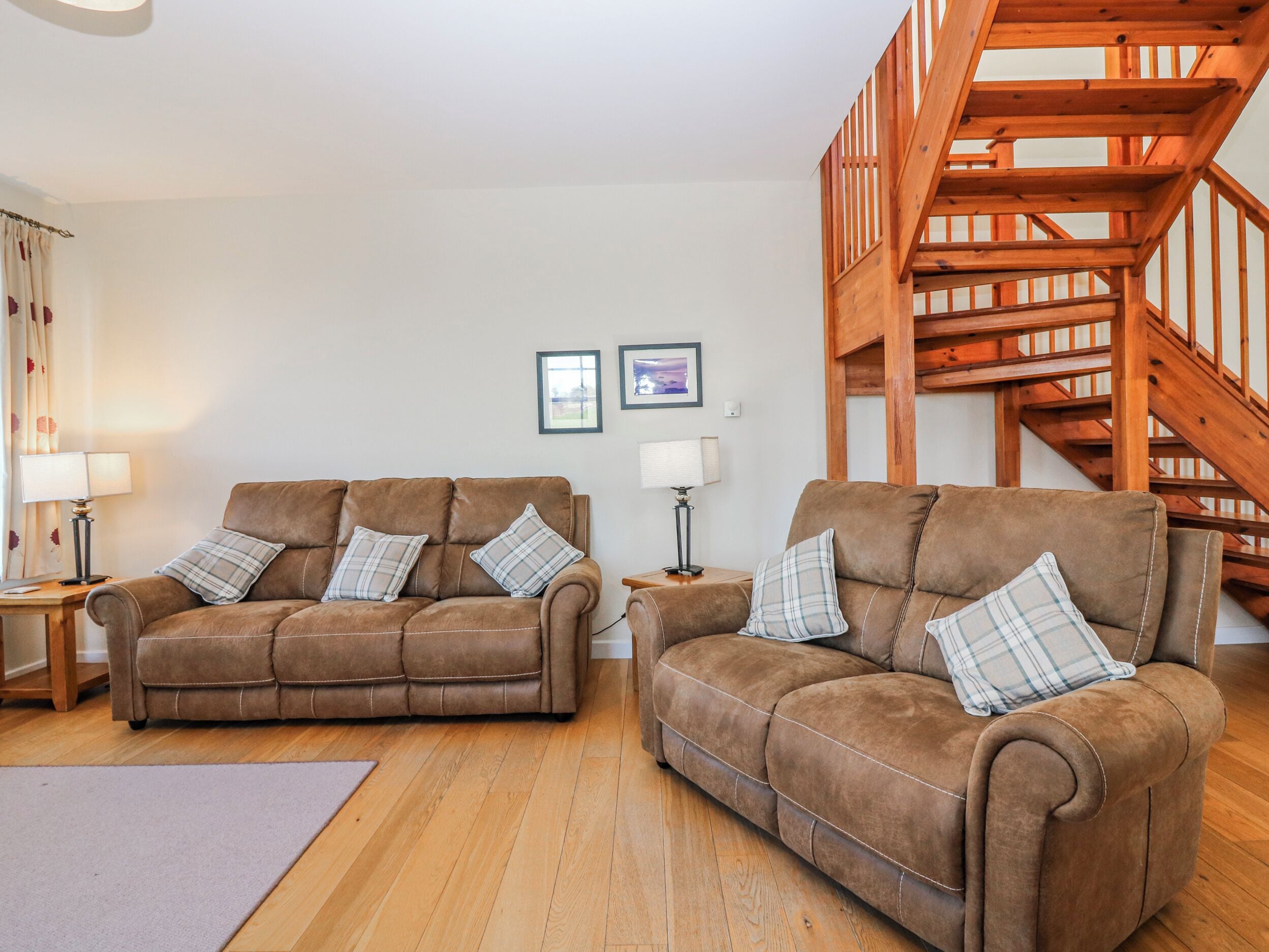 A living room with two brown sofas, wooden flooring, a staircase, and framed pictures on the wall.