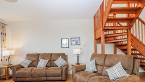 Ein Wohnzimmer mit zwei braunen Sofas, Holzdielen, einer Treppe und gerahmten Bildern an der Wand.