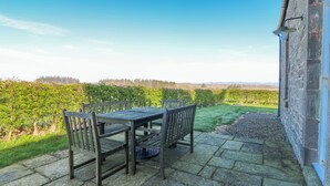 Eine Terrasse mit Tisch und Stühlen, Steinboden und Blick auf einen Weinberg.