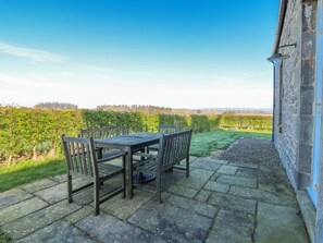 Eine Terrasse mit Tisch und Stühlen, Steinboden und Blick auf einen Weinberg.