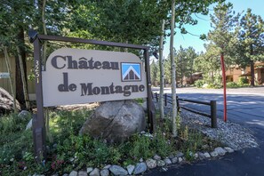 A sign for Chateau de Montague with a mountain icon, surrounded by greenery and a paved area. - Pet-Friendly & Remodeled, Gas Grill, Near the New Rec Center, On-site Pool (Mammoth Lakes)