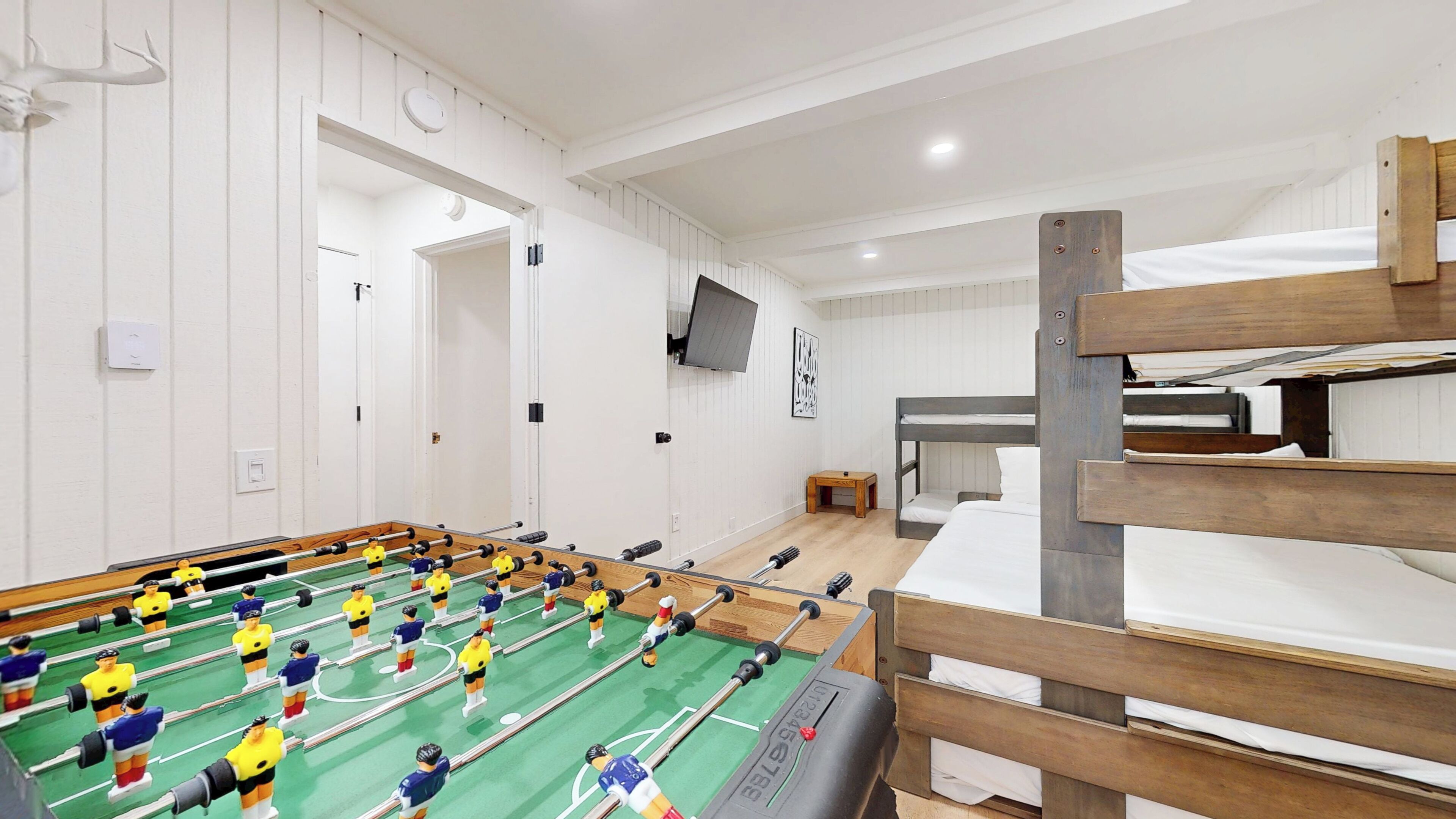 Een kamer met een tafelvoetbaltafel, stapelbedden, een televisie en een deur naar een andere kamer.