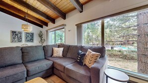 Ein modernes Wohnzimmer mit einer Eckcouch, großen Fenstern und Blick auf ein Außenbecken.
