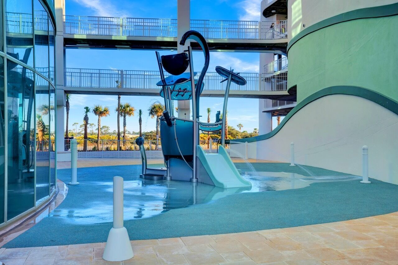 Un espace de jeux aquatiques avec des toboggans et une piscine à vagues, entouré d’un bâtiment en verre doté de balcons.