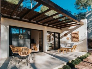A modern house with a covered patio, wicker furniture, and a stone wall.