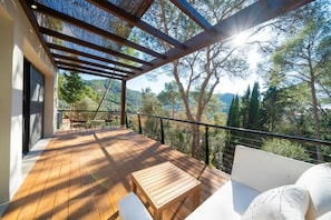 A wooden deck with a table and chairs, a sofa, and a view of trees and hills.