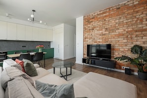 A modern living room with a brick wall, a flat-screen TV, a sofa, a coffee table, and a dining area with chairs and a table. - ShortStayPoland Budki Szczęśliwickie (Warszawa)