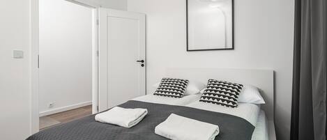 A modern hotel room with a neatly made bed, a framed artwork on the wall, and a door leading to another room.