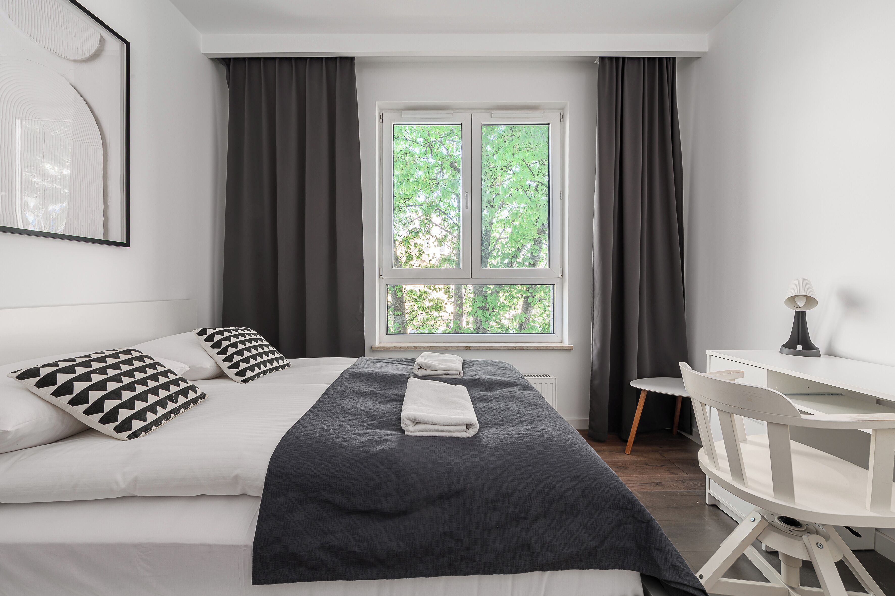 A bedroom with a bed, a desk, and a window with curtains.