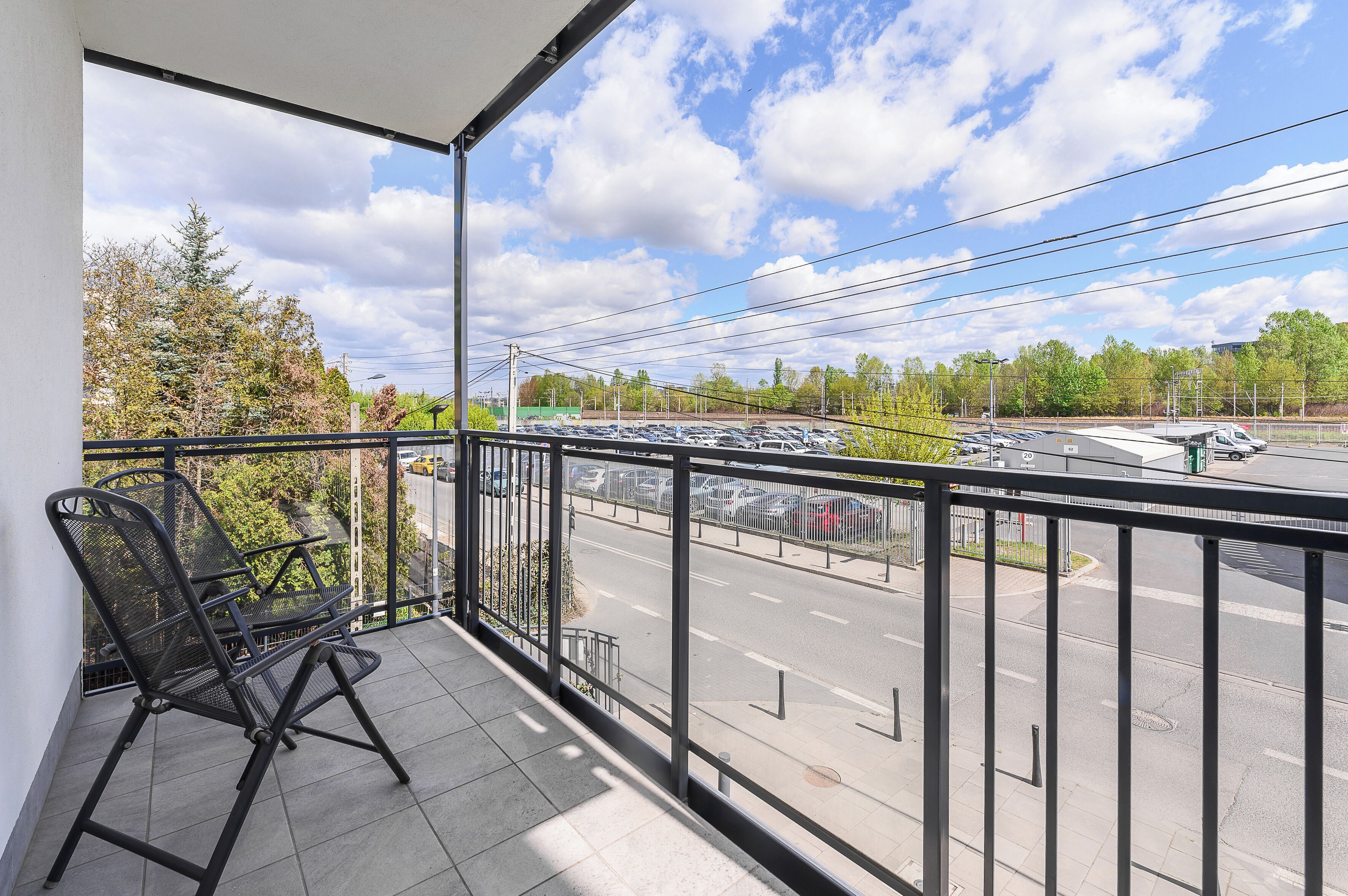 En balkon med en stol og udsigt til en parkeringsplads, under en klar himmel.