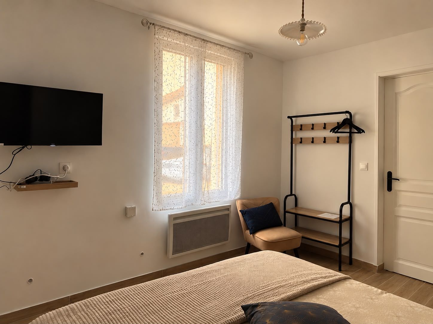 Une chambre à coucher avec un lit, une chaise, un téléviseur fixé au mur, un radiateur et une porte.