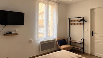 Une chambre à coucher avec un lit, une chaise, un téléviseur fixé au mur, un radiateur et une porte.