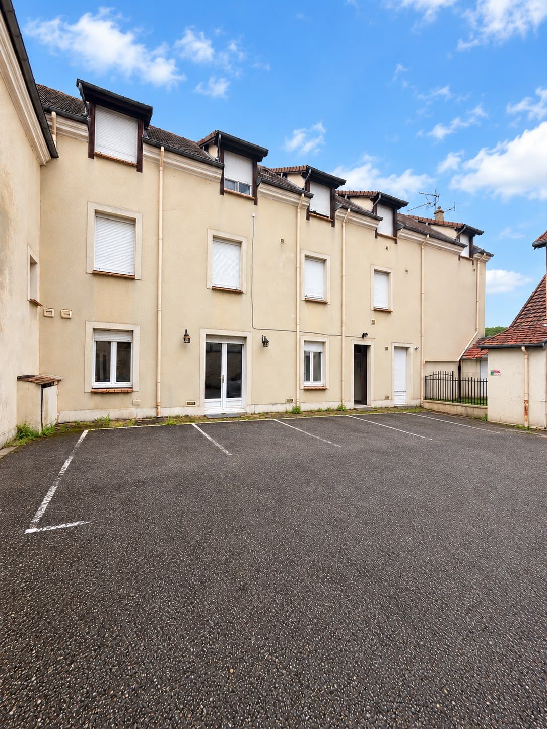 Une rangée d’immeubles d’appartements de couleur beige, avec un parking devant.