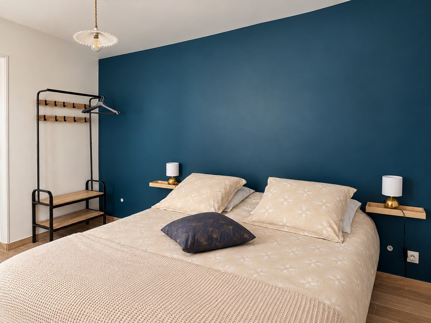 Une chambre à coucher comprenant un lit, deux tables de chevet, un luminaire suspendu et un porte-manteau.