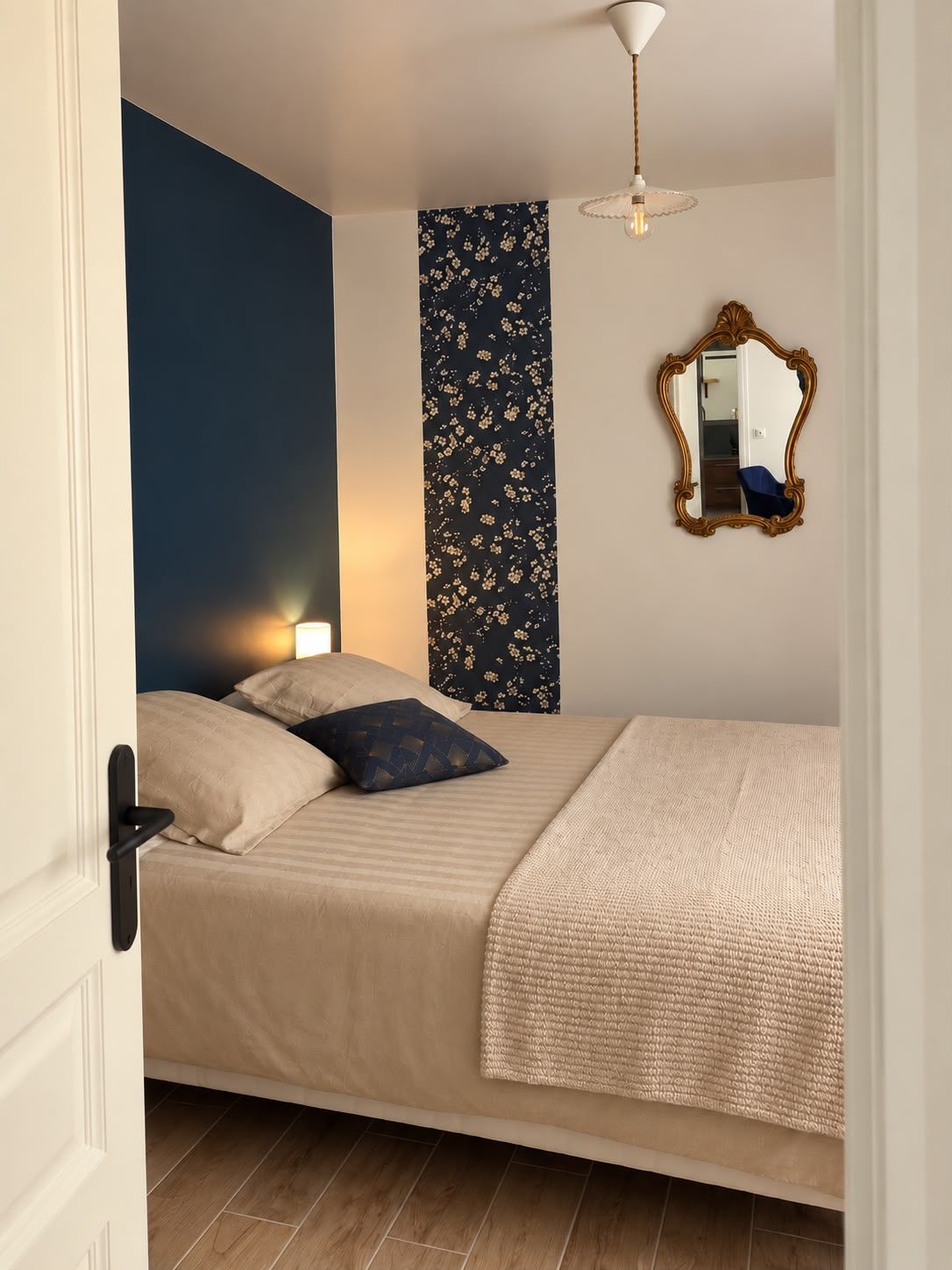 Une chambre à coucher avec un lit, un miroir et un mur orné d’un motif floral.