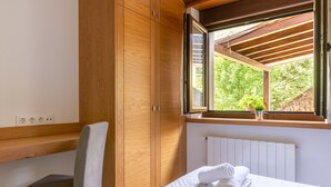 Un dormitorio con un armario de madera, una ventana con vista a la vegetación, una cama con una toalla doblada y una silla.