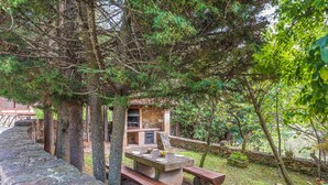 Un muro de piedra, una mesa de picnic y una zona de barbacoa rodeados de árboles.