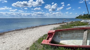 Uma praia com um barco vermelho, mar calmo e céu claro.