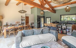 Ein gemütlicher Wohnbereich mit einer Couch, einem Esstisch mit Stühlen, einer Küche mit Kühlschrank und einem großen Fenster.