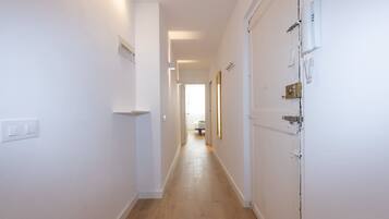 A narrow hallway with white walls, a wooden floor, and a door with a lock and a phone on the wall.