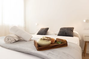 Un lit bien fait, surmontĂ© dâun plateau en bois oĂč reposent une thĂ©iĂšre et des fleurs, une serviette roulĂ©e et un oreiller, le tout posĂ© sur un couvre-lit blanc.