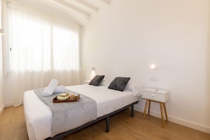 A neatly made bed with pillows, a bedside table, and a small nightstand. - Merceria Suites - Unik Vacation (Tarragona)