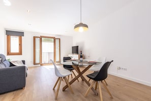Una sala de estar moderna con una mesa de comedor de cristal, un sofá gris y suelo de madera.
