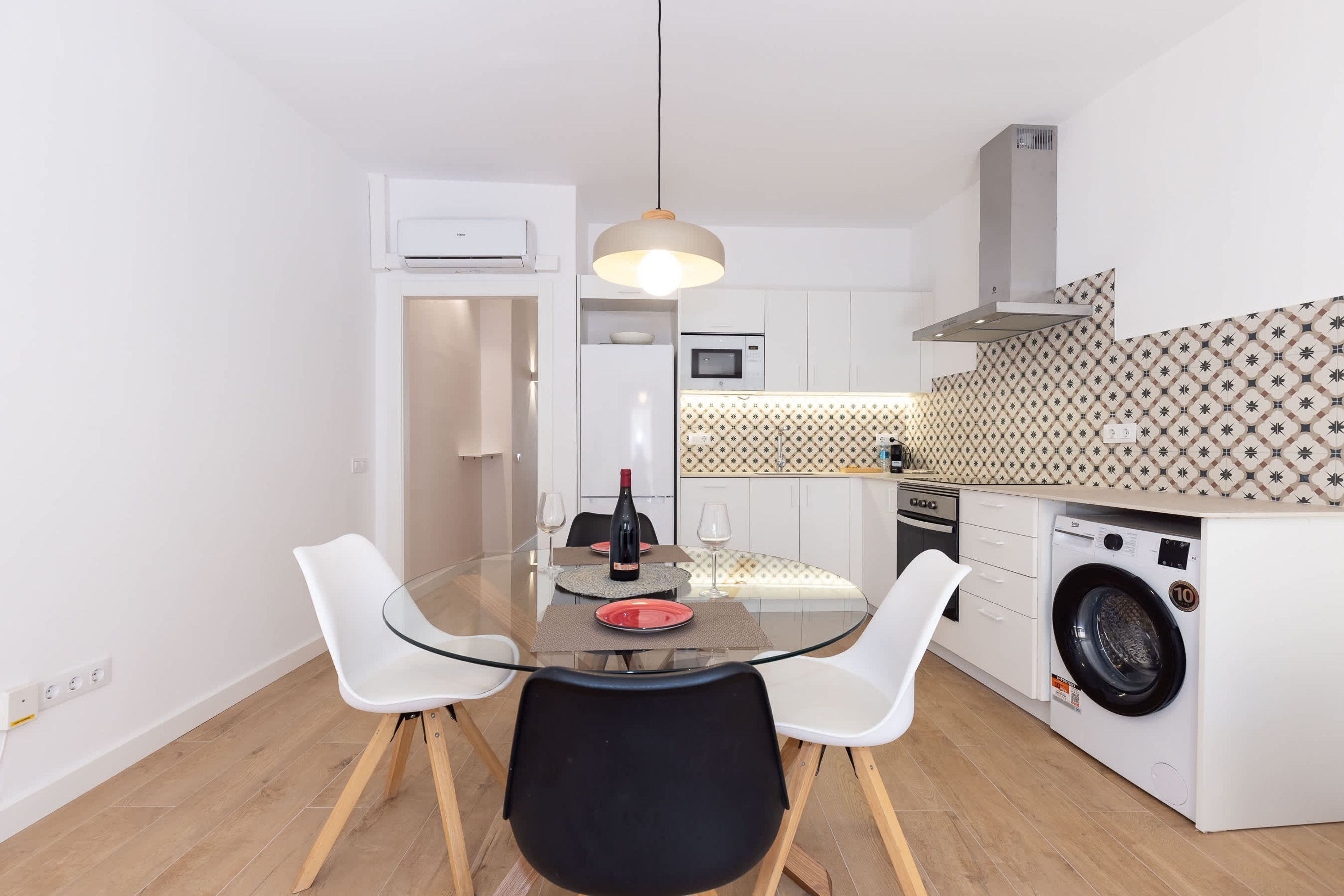 Una cocina compacta con lavadora, una mesa de comedor con sillas e iluminación colgante.
