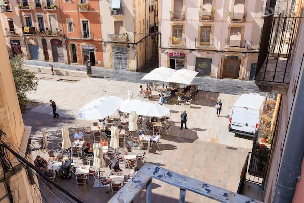 Un cafĂ© en plein air, avec des tables et des parasols, entourĂ© dâimmeubles dotĂ©s de balcons et de plantes.