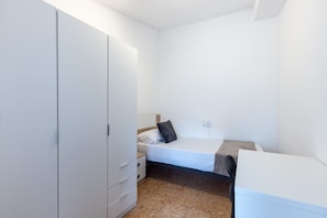 Ein kleines, sauberes Zimmer mit einem Bett, einem Schrank und einem Schreibtisch.