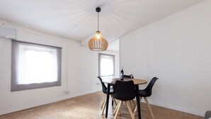 Een eetgedeelte met een ronde tafel, zwarte stoelen, een hanglamp en grote ramen.