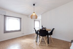 Ein Essbereich mit einem runden Tisch, schwarzen Stühlen, einer Hängelampe und großen Fenstern.