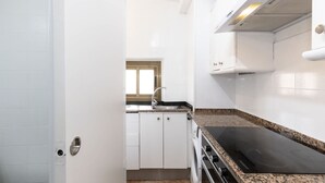 Een keuken met witte kasten, een zwart fornuis en een raam.