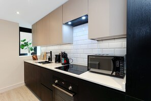A modern kitchen with a black stove, a microwave, and a coffee maker on the countertop. - Perfect Booking 2 Bed Flat With Gym Cinema (Wakefield)