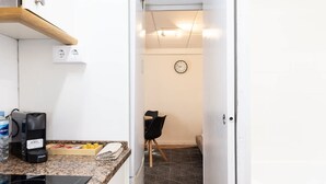 A narrow kitchen with a countertop, a coffee maker, and a microwave. There is a door leading to a dining area with a chair and a table. - Central Part Alta 2 - Unik Vacation (Tarragona)