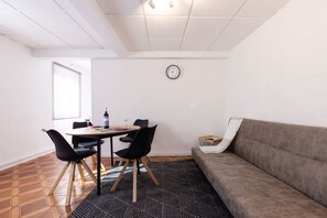 Ein Zimmer mit Esstisch, Stühlen, einer Couch, einer Uhr und einem gemusterten Teppich.