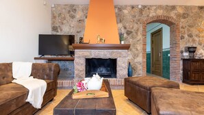 A living room with a stone fireplace, a television, and leather furniture. - Masia Garriga in Tarragona (Alcover)