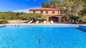 A pool with lounge chairs, a stone building with a tiled roof, and surrounding greenery. - Masia Garriga in Tarragona (Alcover)