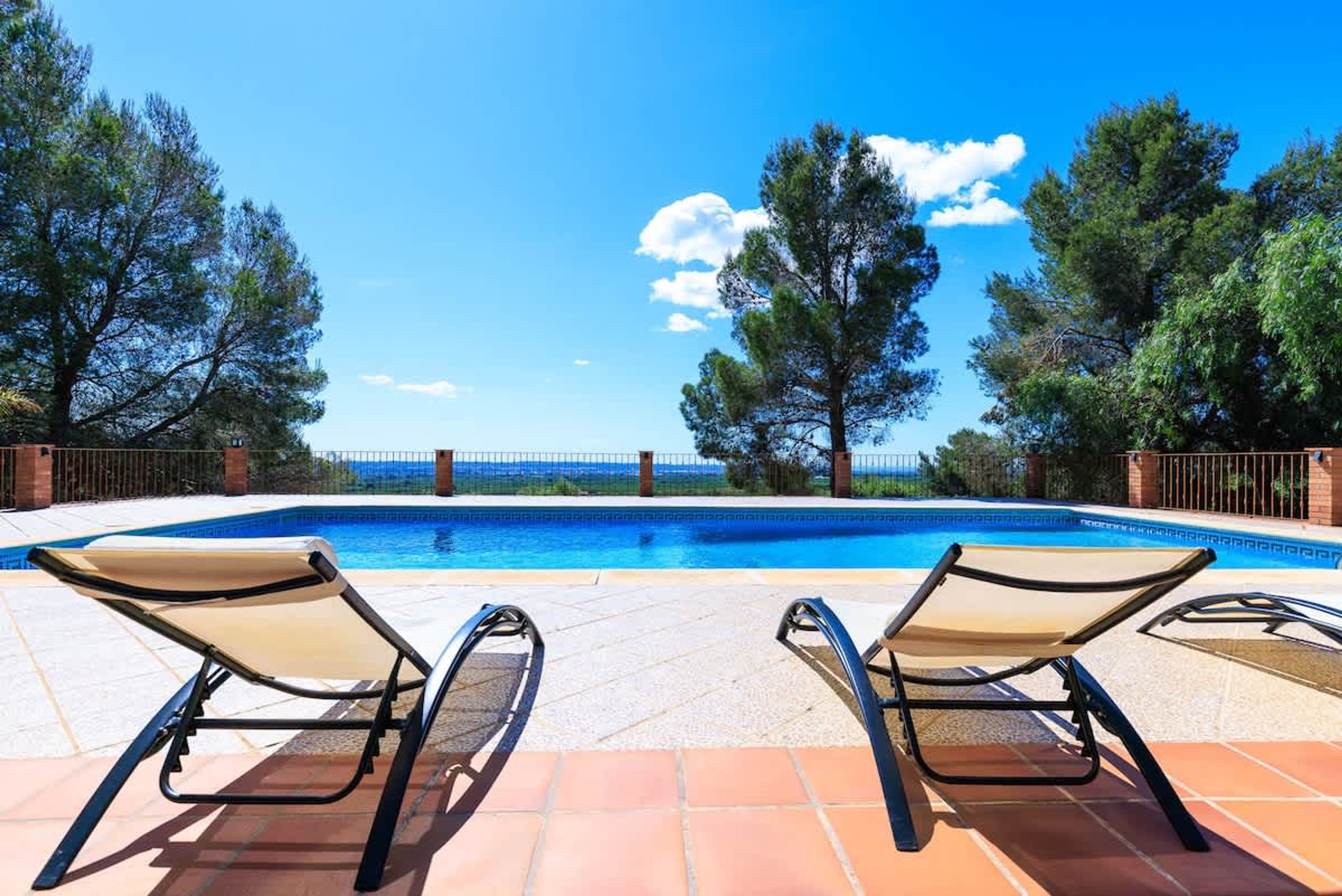 Una piscina con sillones de descanso, rodeada de árboles y un cielo despejado.