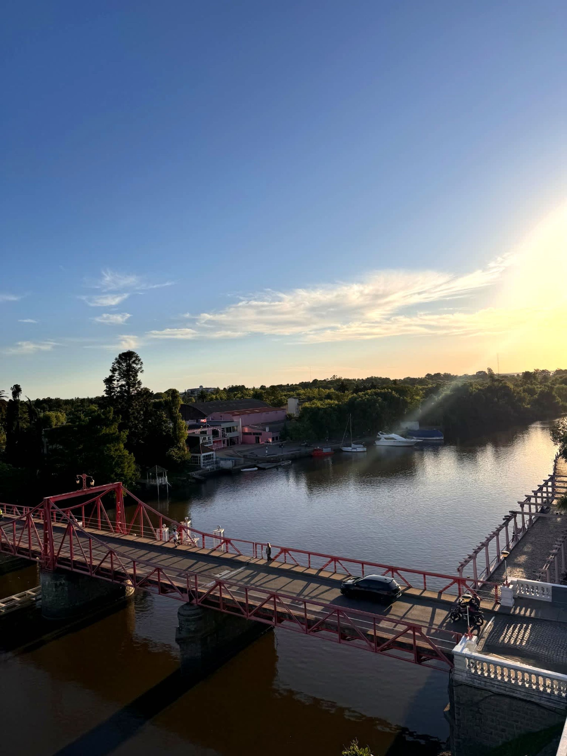 A river with a red bridge, boats, and a building with a red roof.