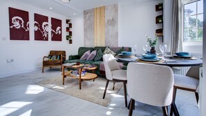 En moderne stue med sofa, stole, spisebord og kunst på væggen.