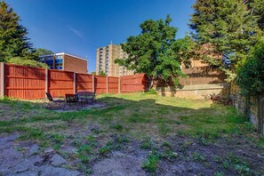 A fenced backyard with a patio table and chairs, a tree, and a building in the background. - Perfect Booking Stylish 3 Bed House in Enfield (Enfield)